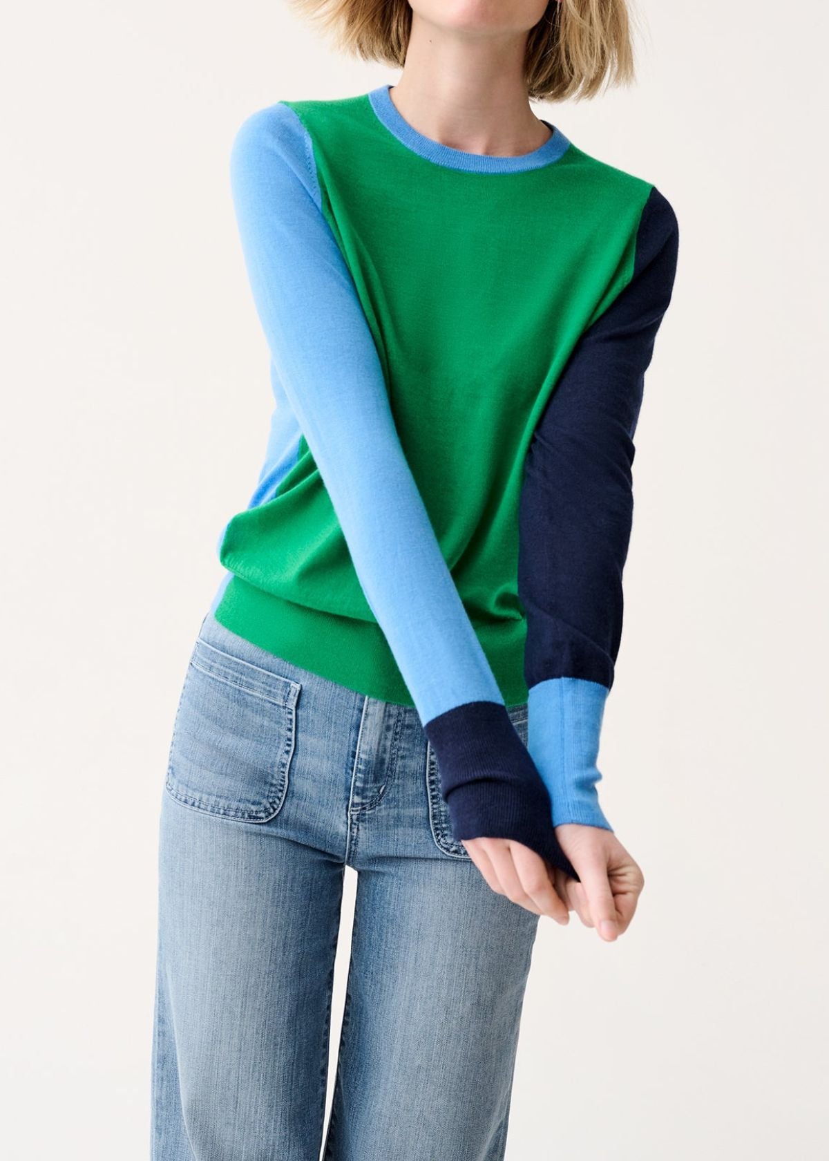 Person wearing a green and blue long-sleeve top with light blue jeans on a white background