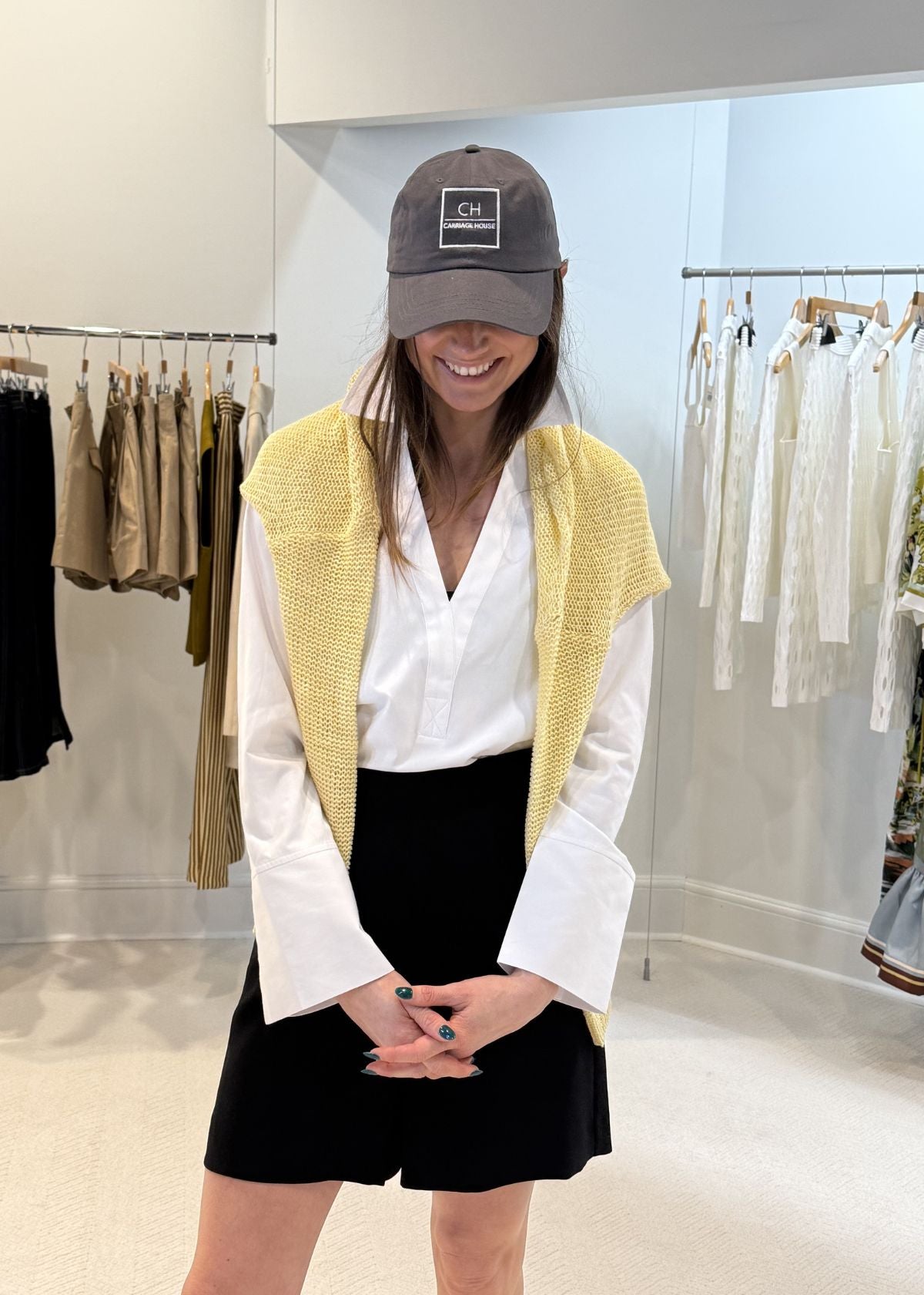 Person wearing a yellow cardigan, white shirt, black shorts, and gray cap in a clothing store.