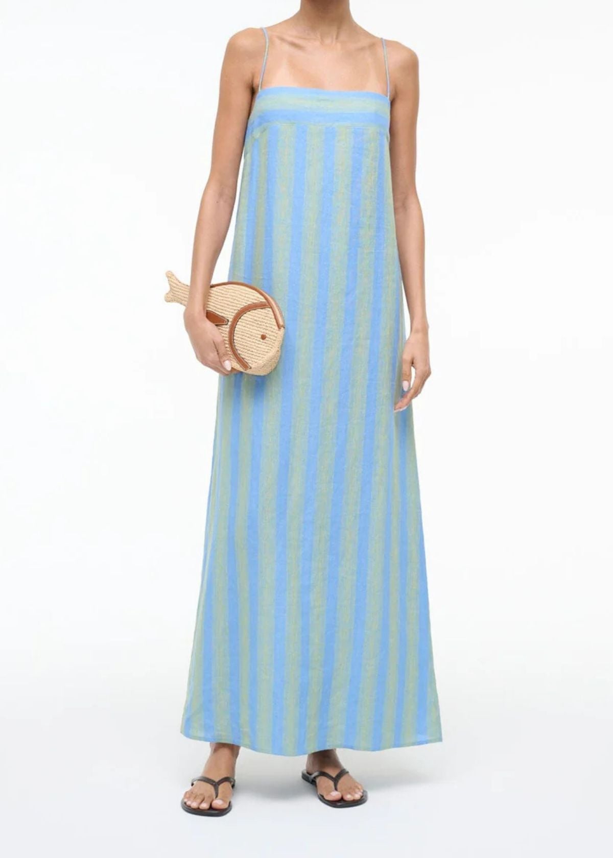 Woman wearing a blue and white striped dress holding a woven handbag on a white background